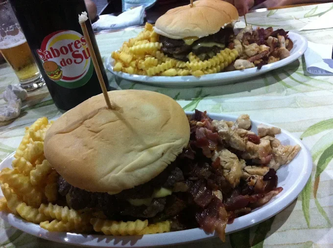 Dois lanches X montados no prato com batata frita, bacon e frango, e um chope Sabores do Sul na mesa